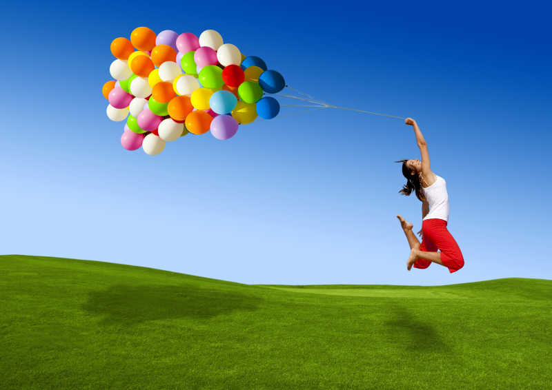 牵着气球的女孩在草地上跳跃
