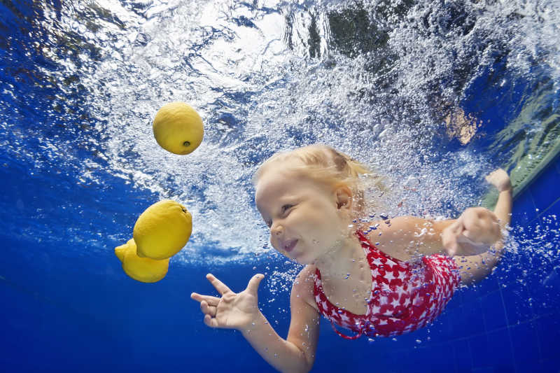 儿童游泳课小女孩跳水和潜水在游泳池与乐趣柠檬水果