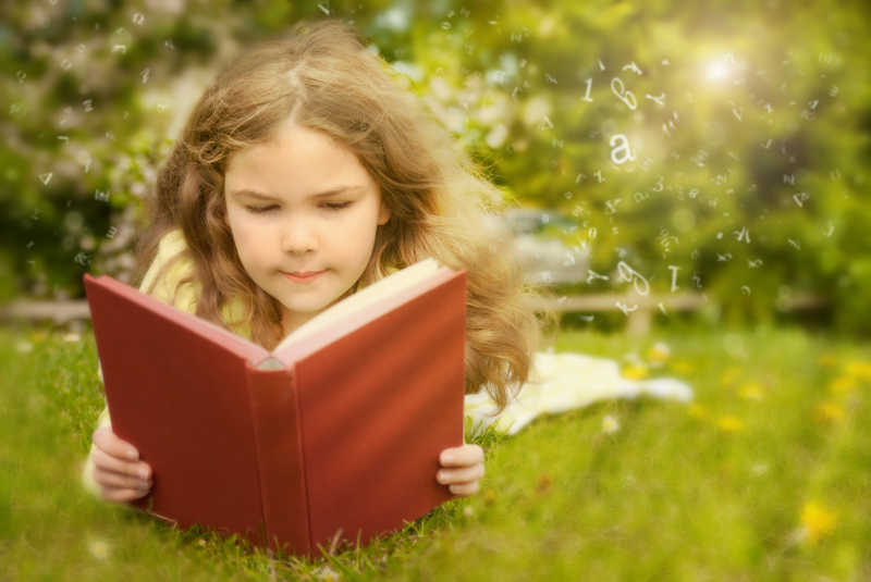 趴在草地上认真看书的小女孩