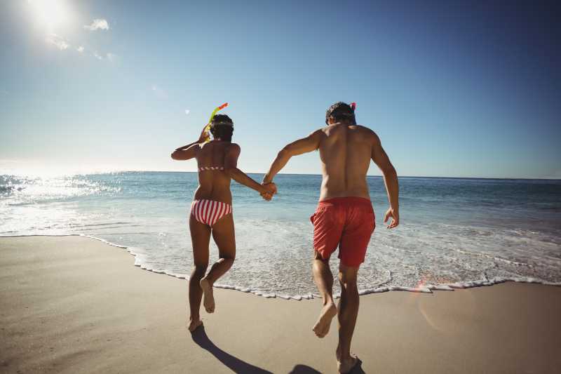 奔跑在海滩上带着潜水面具的手拉手的情侣