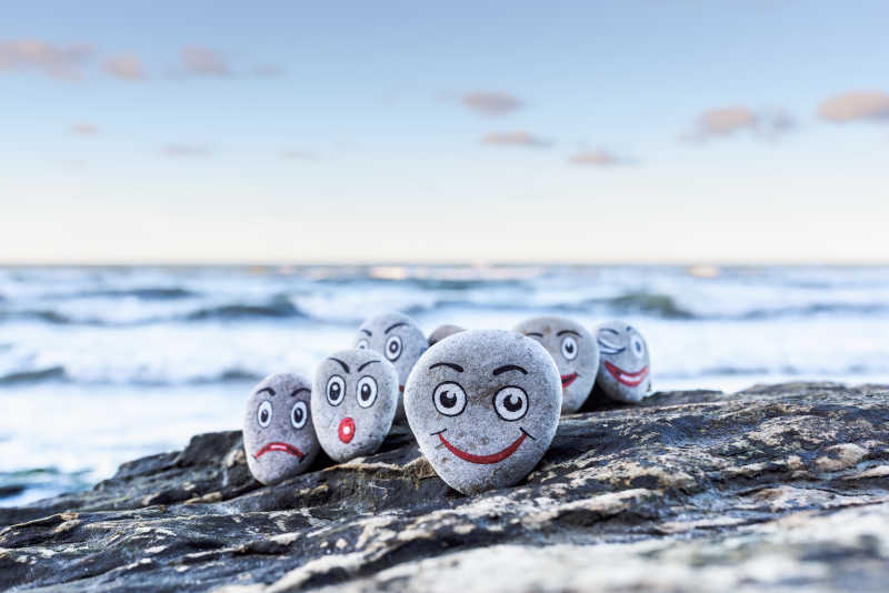 海滩岩石上放着画着笑脸的鹅卵石