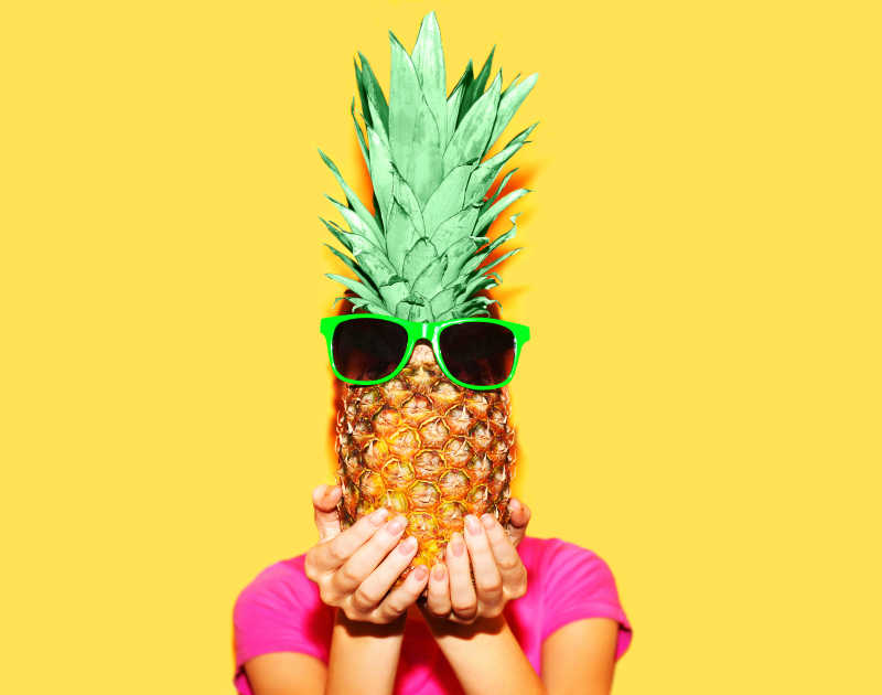 黄色背景下举着带眼镜菠萝的女人