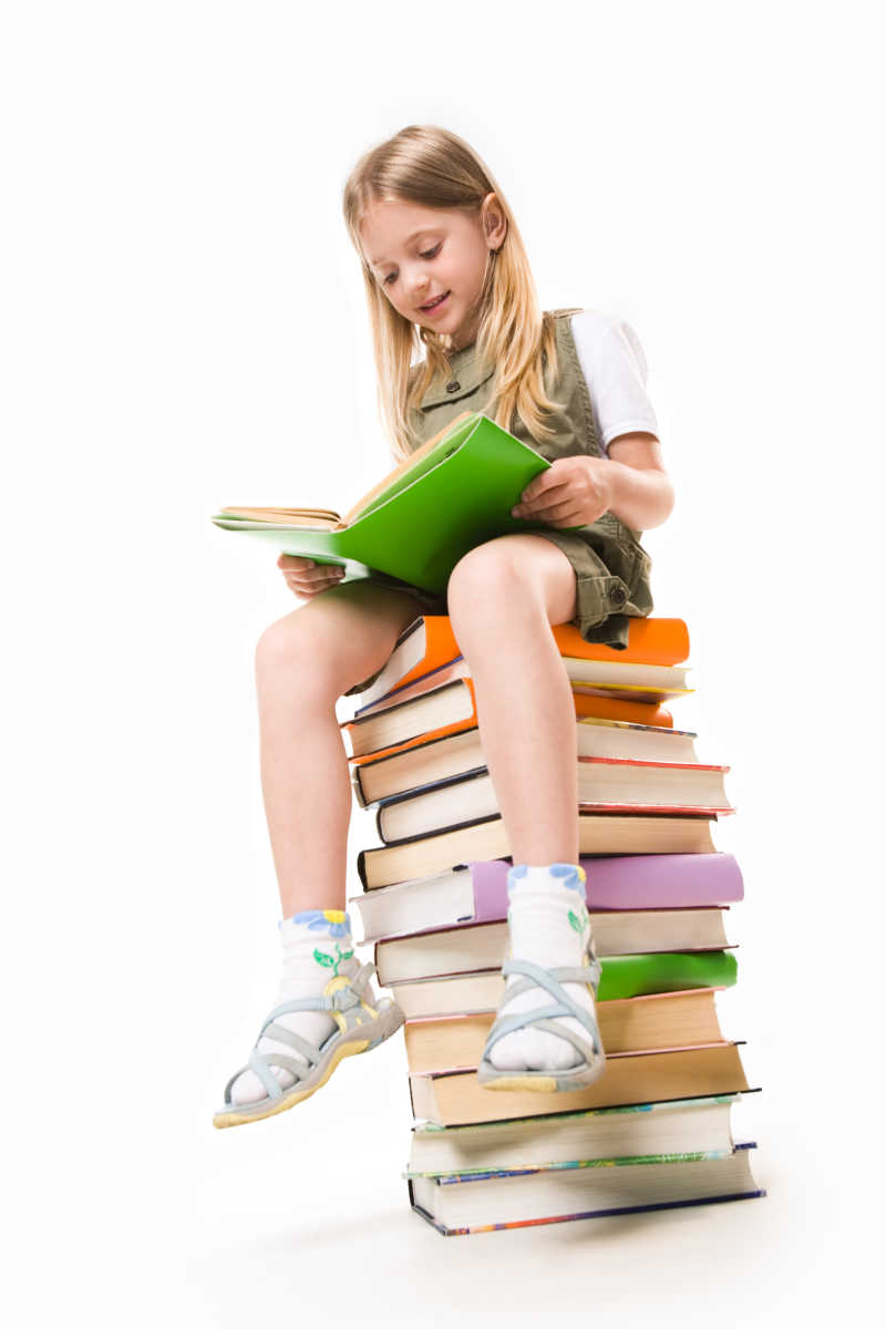 小女孩在一堆书上坐着阅读学习