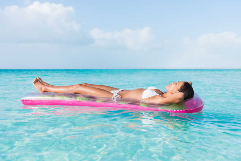 清澈的海水里躺在粉色漂浮垫上晒日光浴的白色比基尼美女