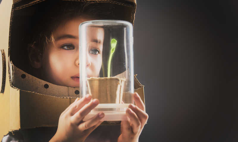 穿着太空服的孩子拿着装在玻璃盒子里的植物