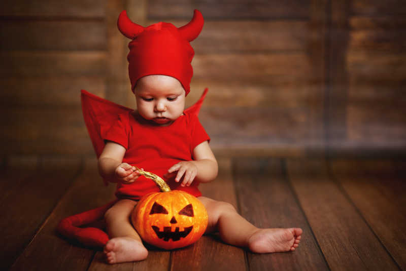 木制背景上玩南瓜灯的恶魔装扮的孩子