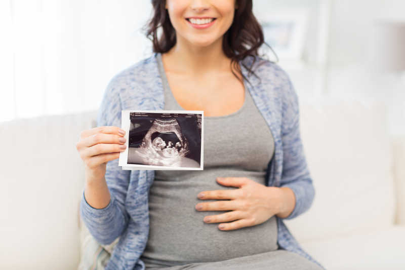 孕妇手里拿着超声波照片露出快乐的微笑