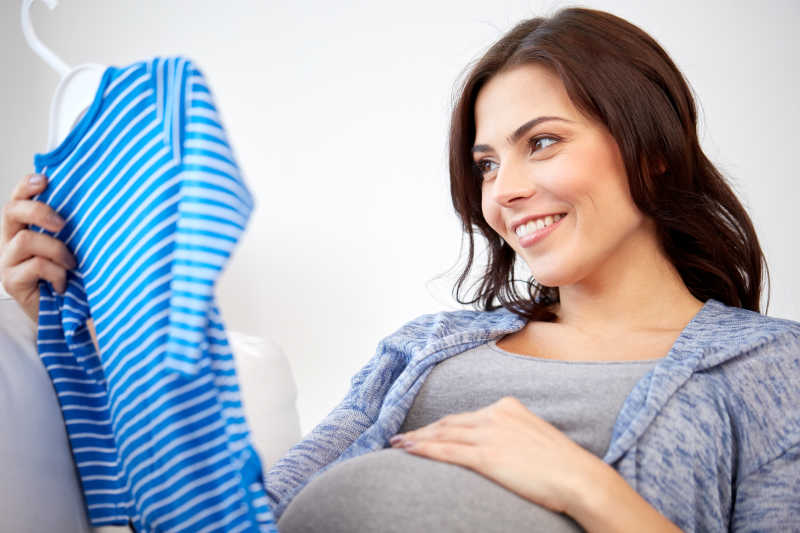看着婴儿服装的快乐的孕妇
