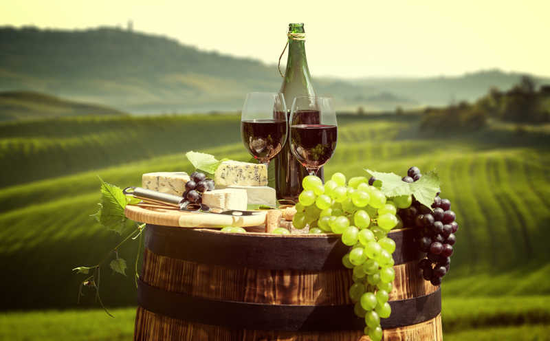 绿色葡萄园背景前的木酒桶和新鲜的葡萄红酒