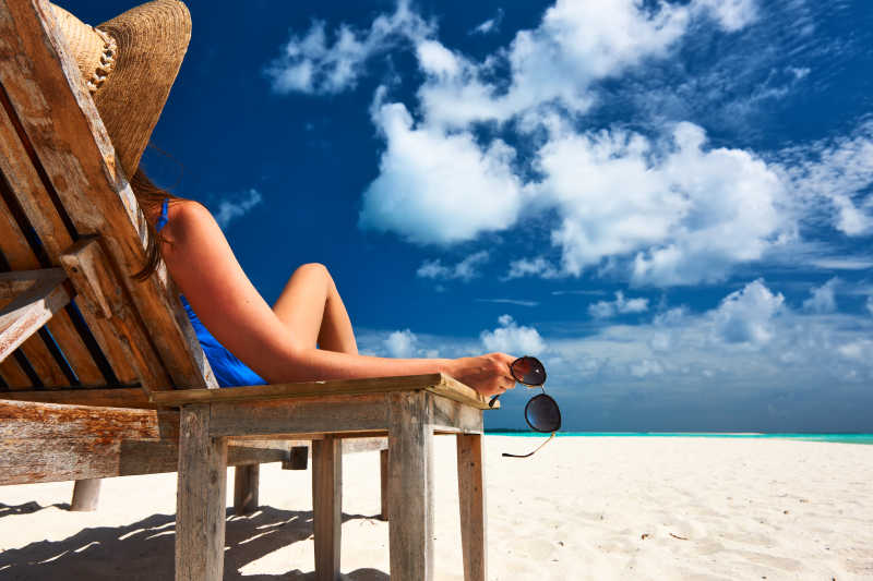 海滩上手拿着太阳镜躺在椅子上的女人