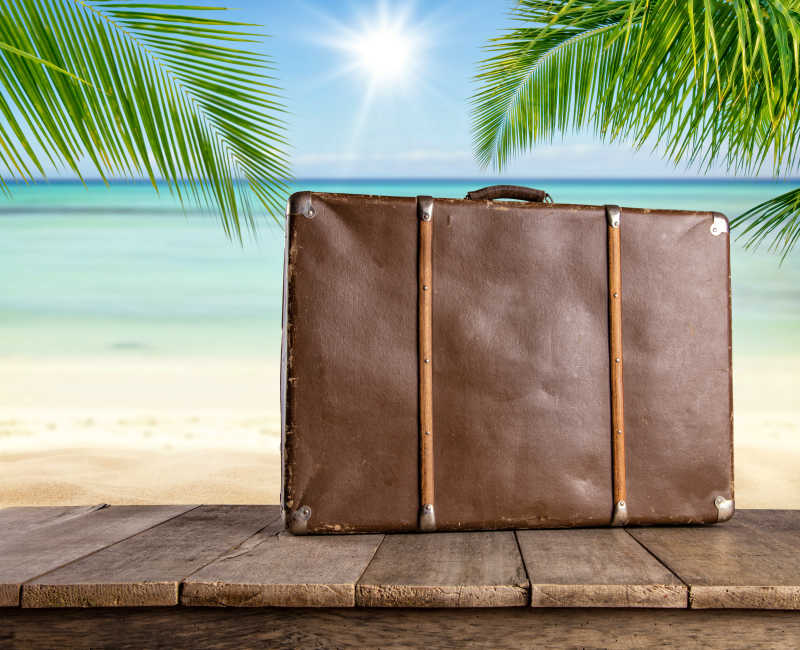 热带海滩背景前的木桌上的旧旅行行李箱