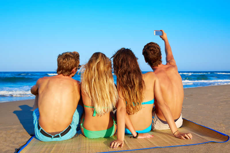 坐在沙滩面朝大海的朋友情侣组合后视图