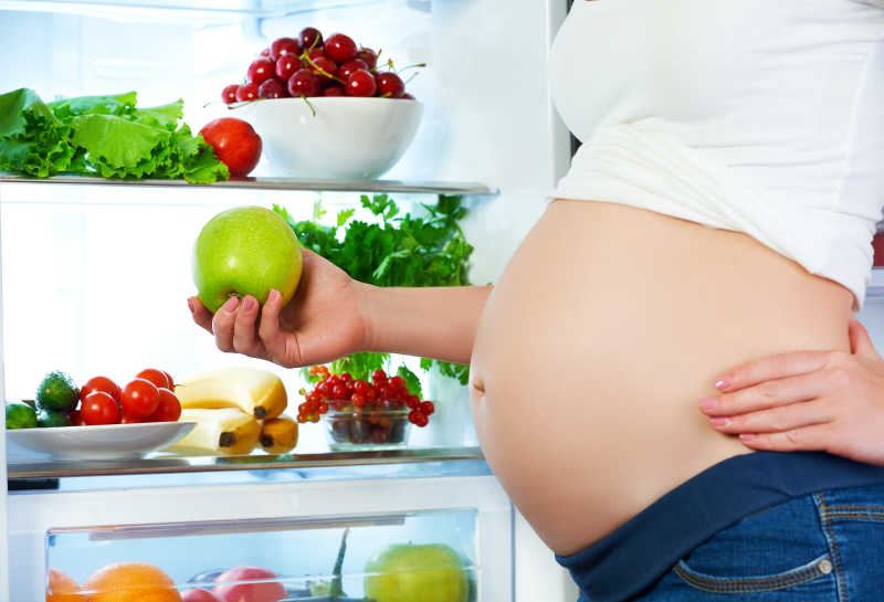 冰箱边吃蔬菜的孕妇