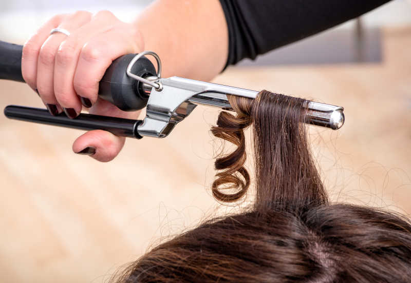 发型师使用卷发熨斗在女客户的棕色长发中固定小环