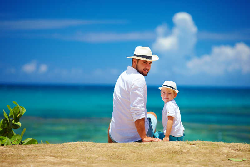 暑假快乐的父亲和儿子坐在海边向后看