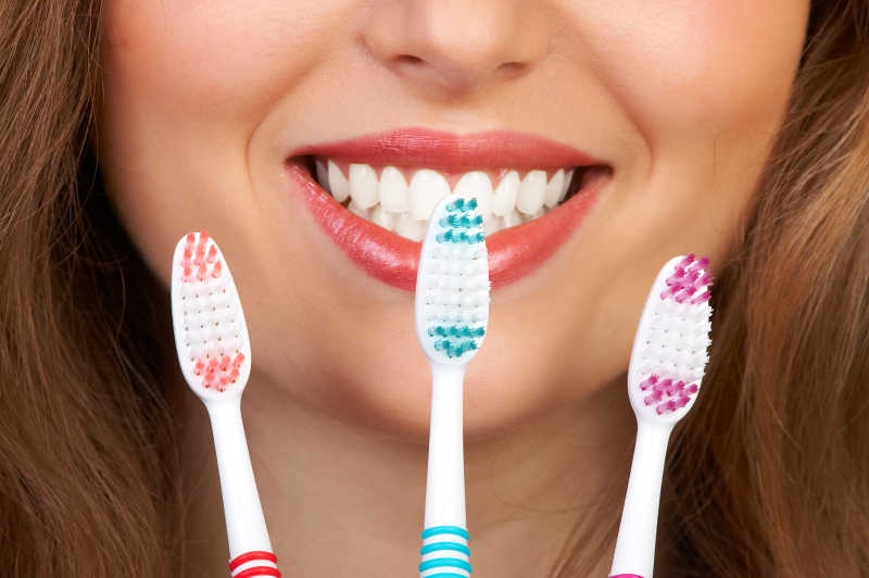 手拿三支牙刷的美女露出洁白的牙齿