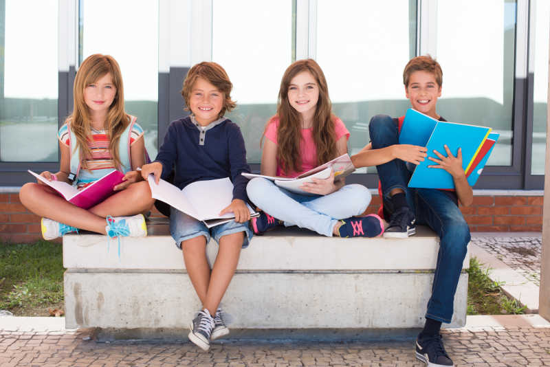 坐在校园里的石椅上看书的四个微笑的学生