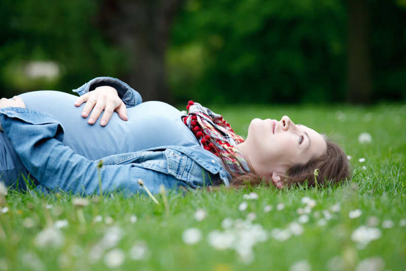 躺在绿色草地上的年轻孕妇