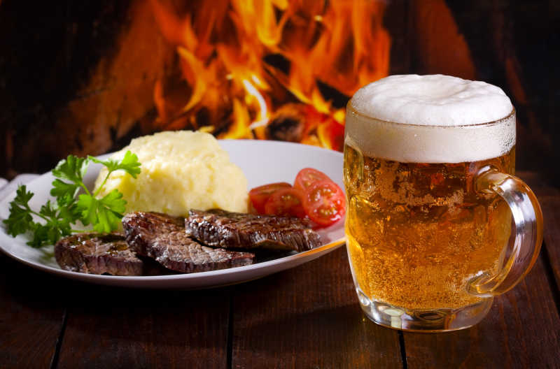篝火旁的木桌上的牛排和啤酒