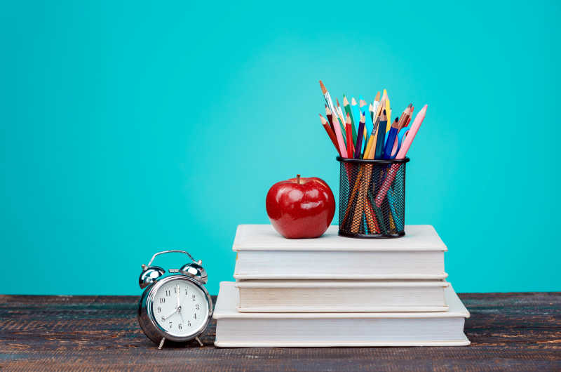 蓝色背景前桌子上的学习用品和苹果