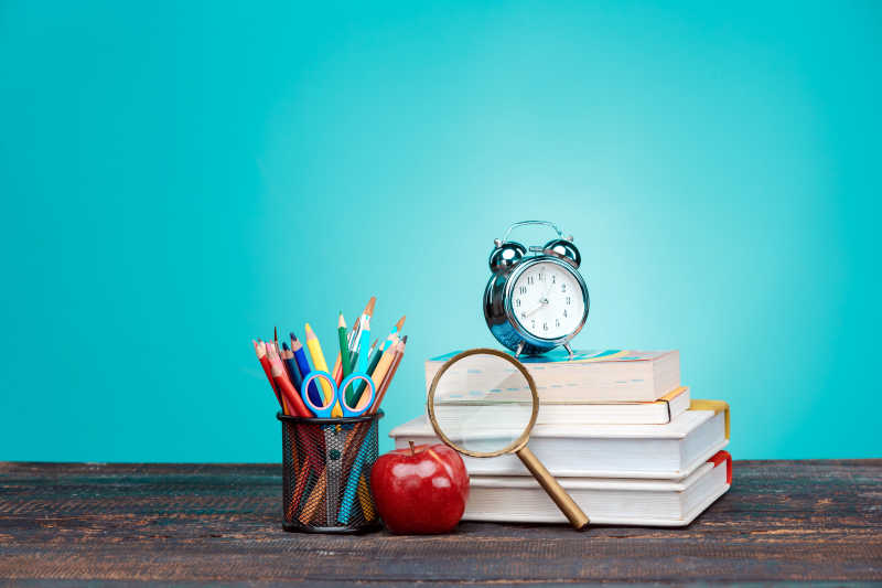 蓝色背景前桌子上的红苹果和学习用品