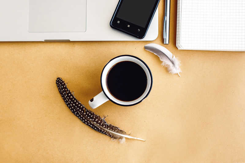 笔记本电脑旁边的咖啡杯和羽毛