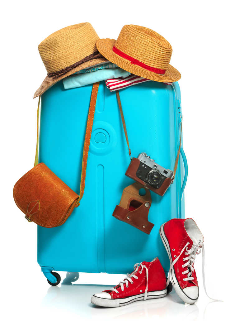 白色背景下挂着背包运动鞋和遮阳帽的蓝色行旅箱