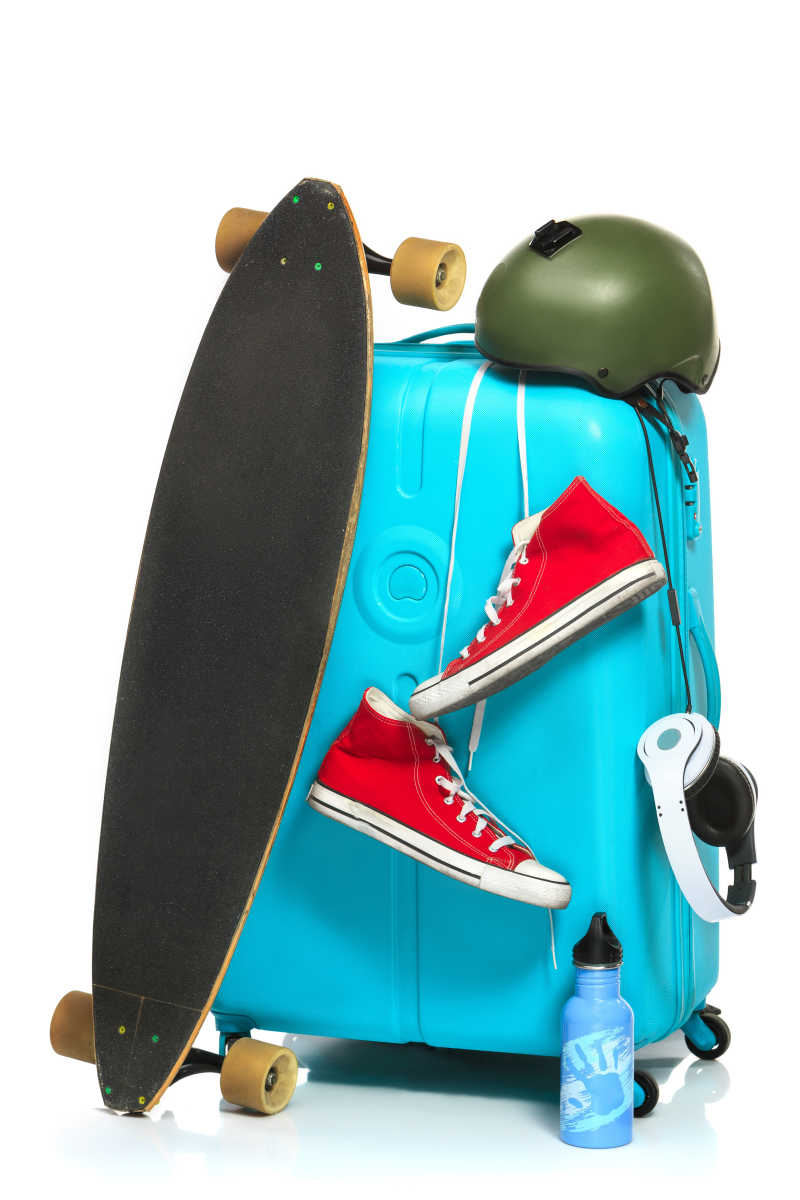 白色背景下挂着运动鞋耳机和滑板的蓝色行李箱