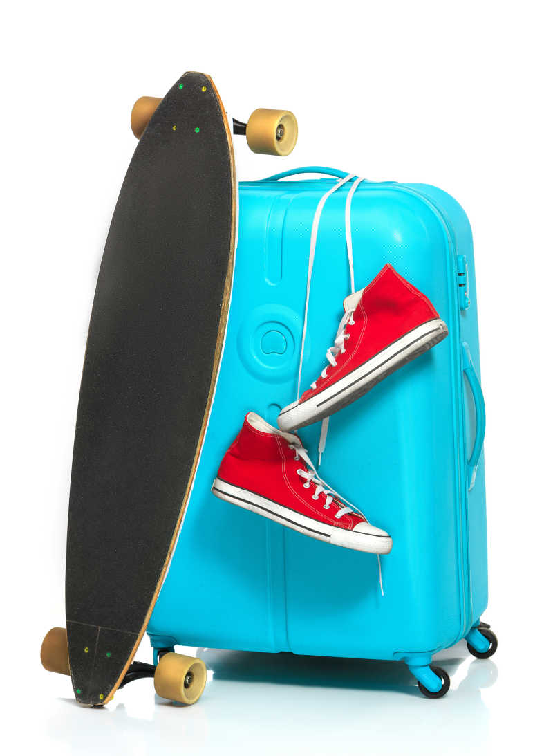 白色背景下靠着滑板和运动鞋的蓝色旅行箱