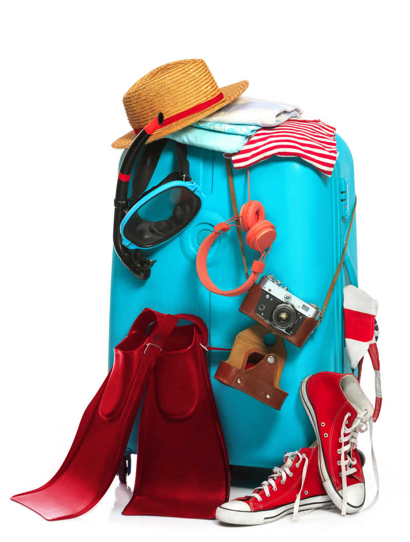 白色背景下挂着相机耳机运动鞋帽子以及游泳鞋的蓝色旅行箱