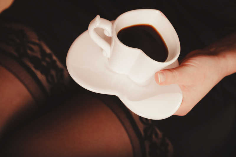 黑色背景下美女端着一杯心形咖啡杯装着的一杯咖啡