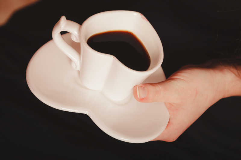 黑色背景下端着心形白色咖啡杯的美女手部