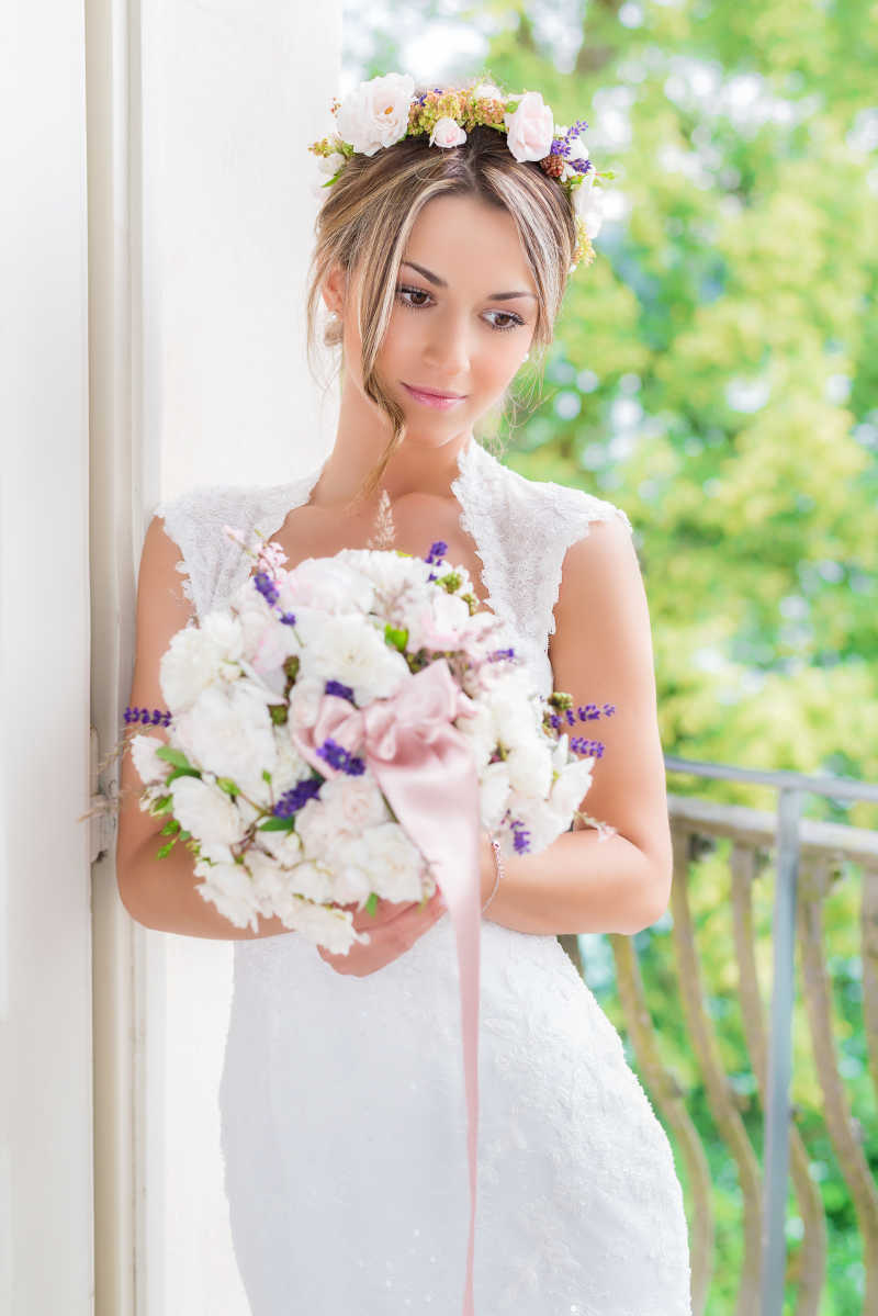 倚在白墙上拿着鲜花的漂亮新娘