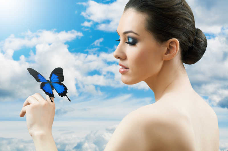 蓝天白云背景上的女人和手中的蓝色蝴蝶