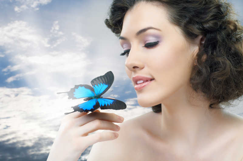 自然背景上美丽女人和手上的蓝色蝴蝶