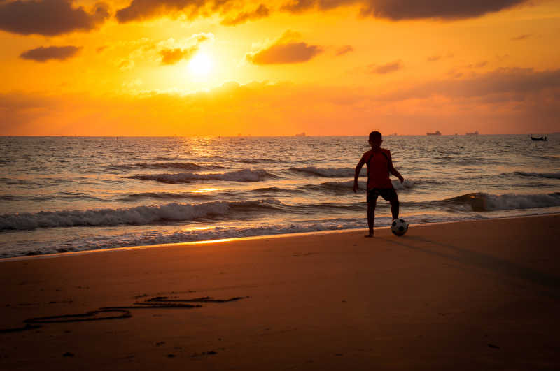 男孩在夕阳下的沙滩上踢球