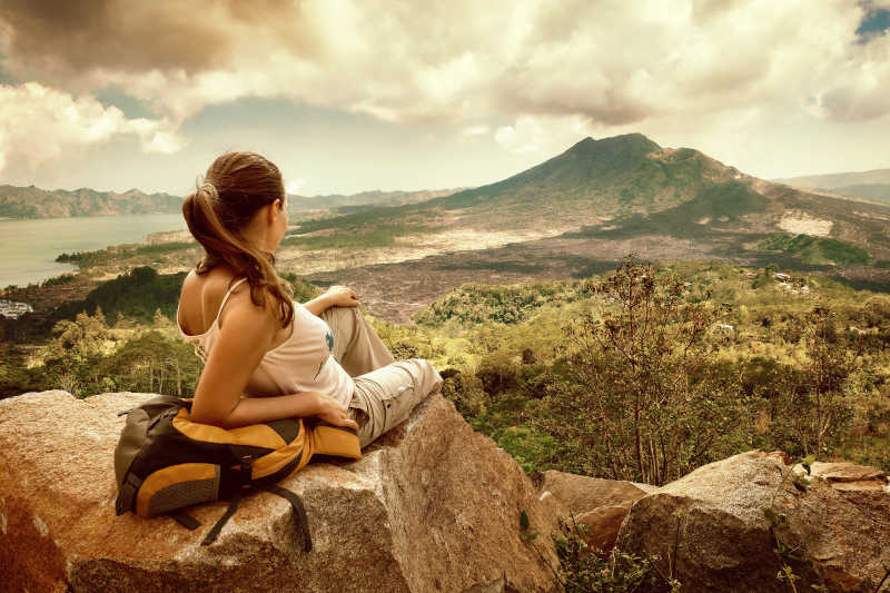 一名妇女背包客坐在悬崖边上看着巴都尔火山