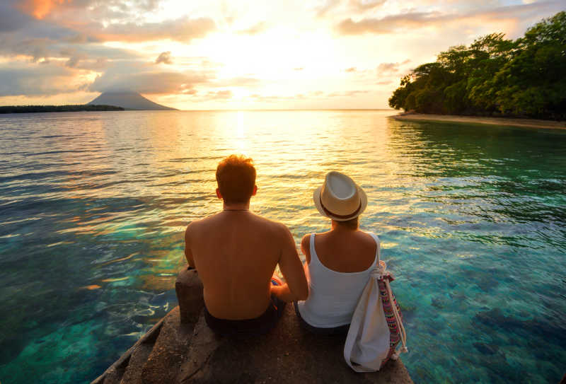 在多彩的夕阳下坐在码头上的一对幸福情侣的背影