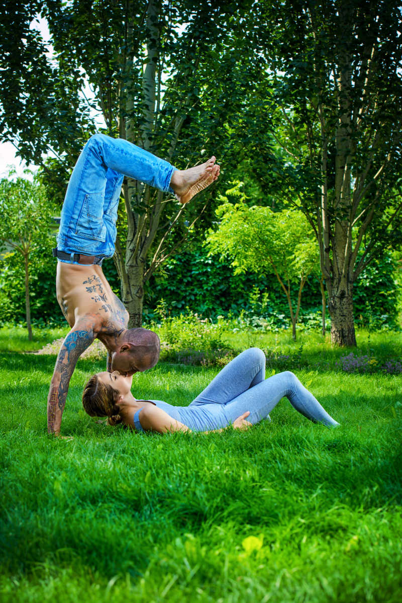 草地上做情侣瑜伽的幸福的年轻情侣