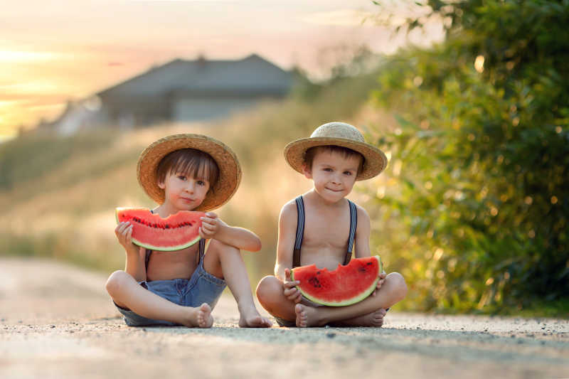 两个可爱的小男孩坐在路上吃西瓜