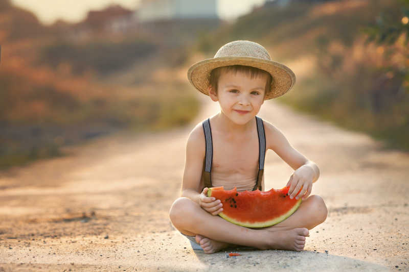 在乡村小道上吃西瓜的可爱的小男孩