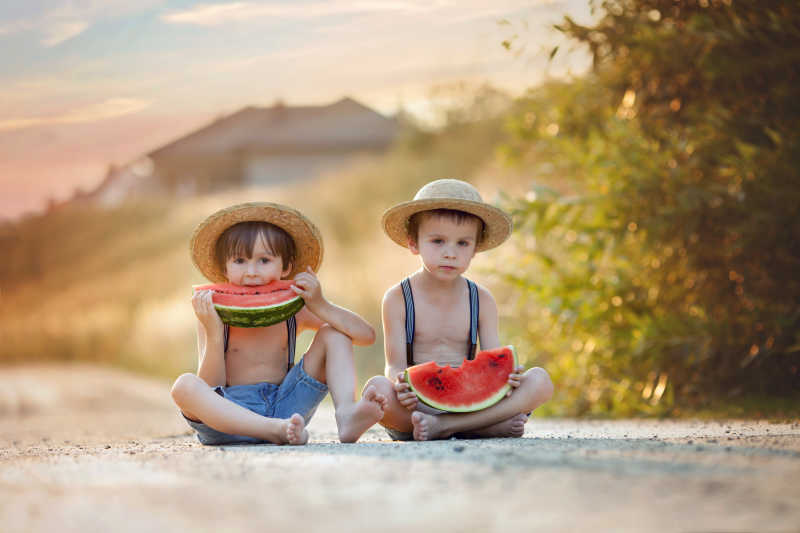 坐在乡村小道上吃西瓜的两个可爱的小男孩