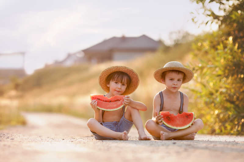 两个可爱的小男孩坐在路中间吃西瓜