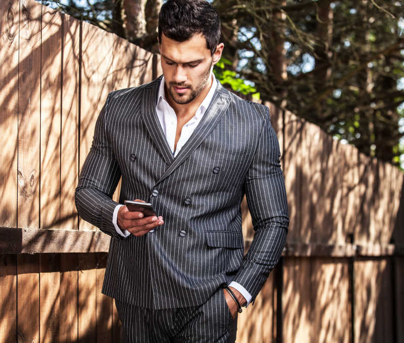 优雅的英俊男子穿着古典灰色西装在看手机