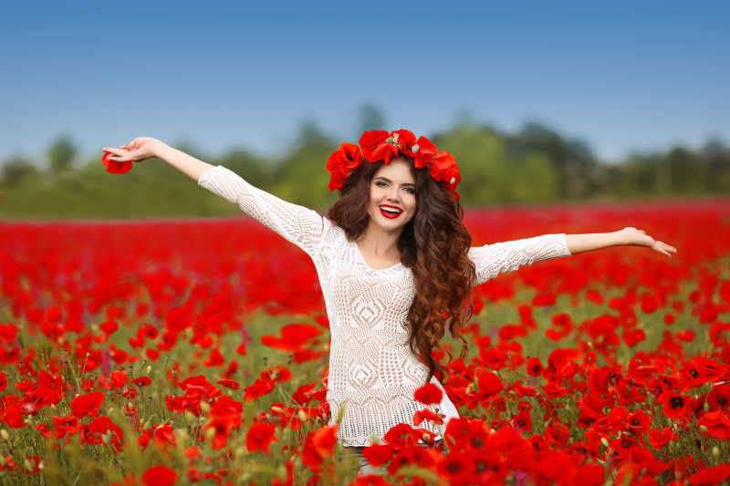 美丽的女人在红色罂粟花田中张开双臂