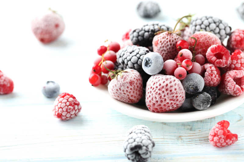 白色木板上美味的草莓蓝莓覆盆子以及越桔等多汁的冰冻水果