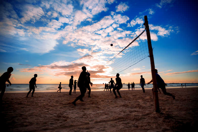 日落的沙滩上打排球的人剪影