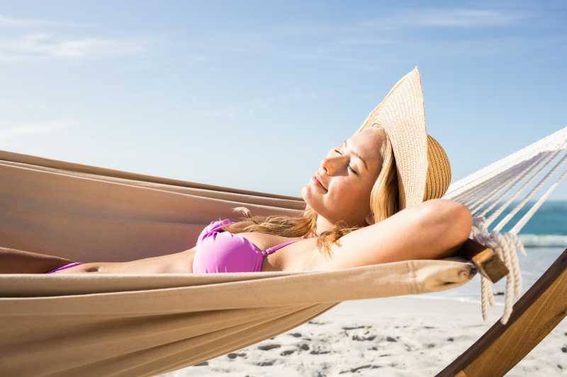 穿着紫晴朗的海边色比基尼躺在吊床上晒日光浴的美女