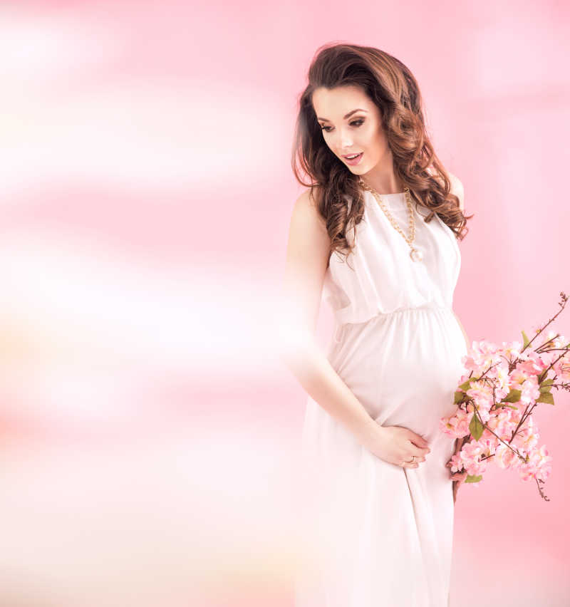 粉色背景下穿着粉色衣服拿着花束的漂亮孕妇