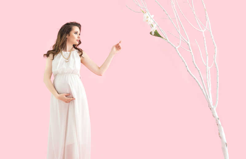 粉色背景下穿着白色裙子的漂亮孕妇